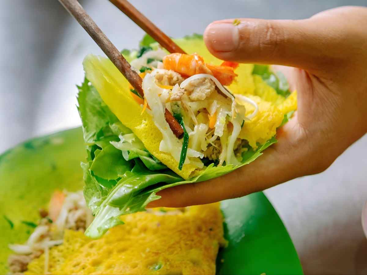 Cách ăn bánh xèo kết hợp rau rừng tạo trải nghiệm hương vị hài hòa. 