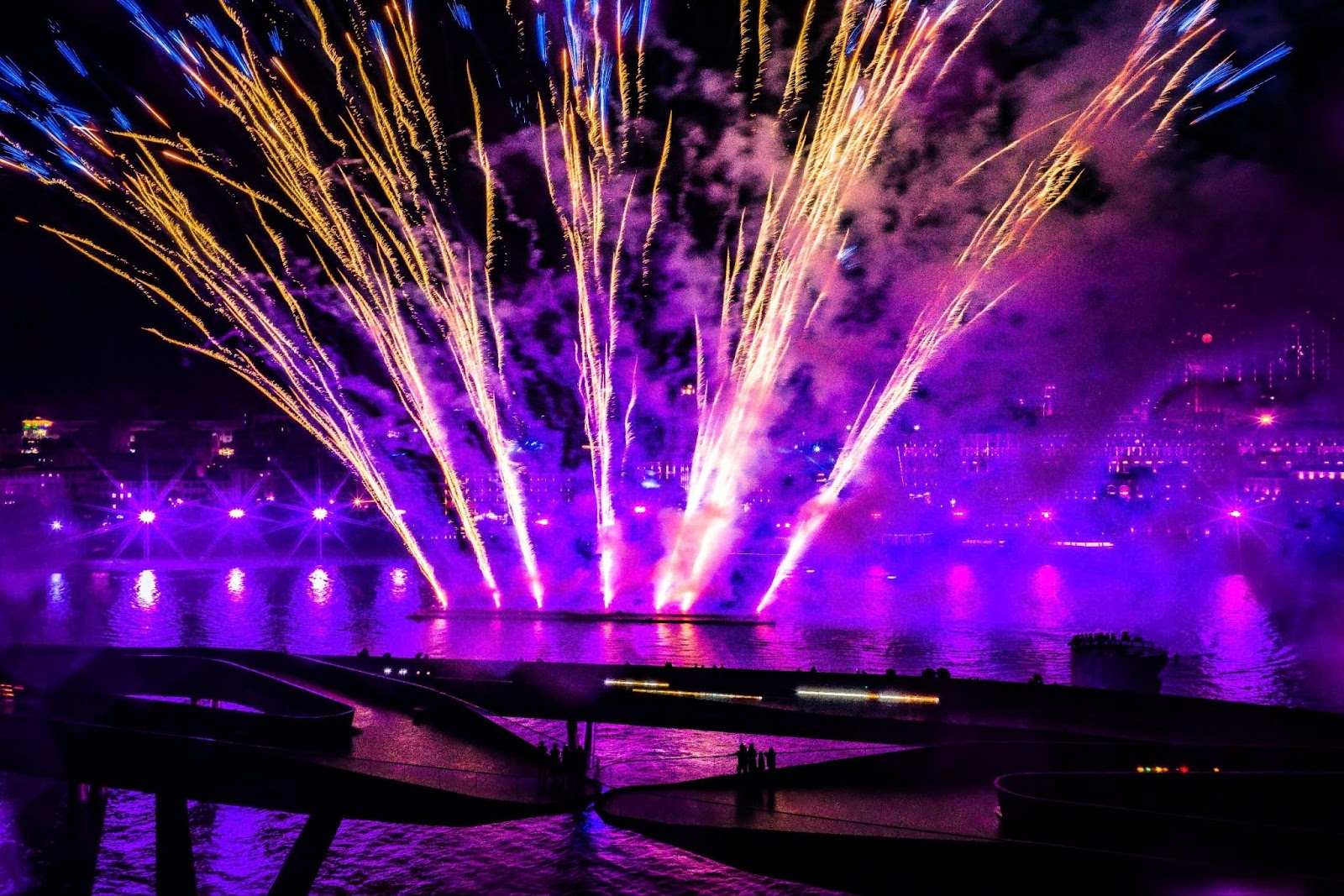 Symphony of the Sea, featuring buildings illuminated by lights and a dazzling fireworks display over the water 